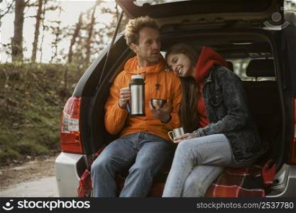 front view couple enjoying hot beverage trunk car