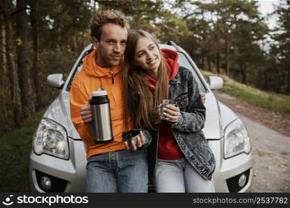 front view couple enjoying hot beverage while sitting hood car outdoors