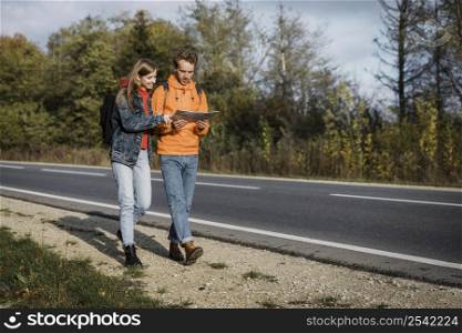 front view couple holding map walking along road