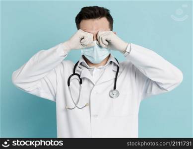 front view doctor with medical mask rubbing his eyes