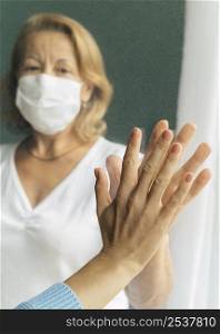 front view elder woman with medical mask touching hand with someone through window
