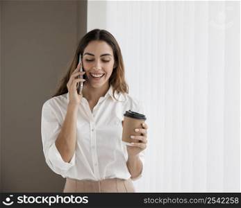 front view elegant businesswoman talking phone while holding coffee cup
