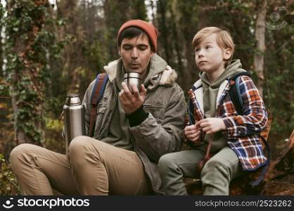 front view father son having hot tea outdoors nature