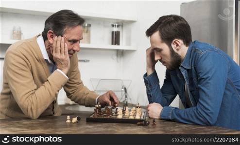 front view father son playing chess kithcen