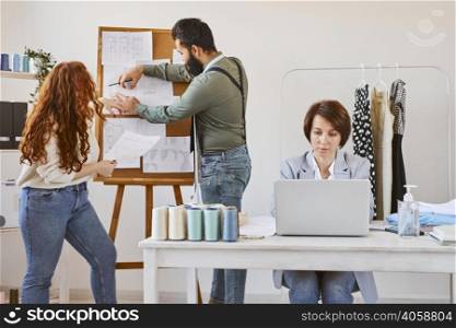 front view female fashion designer working atelier with laptop colleagues