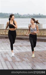 front view female friends having fun while jogging together outdoors