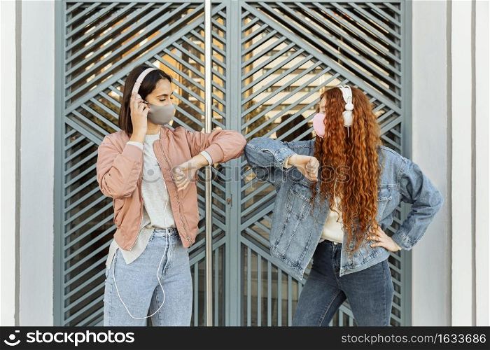 front view female friends with face masks outdoors doing elbow salute