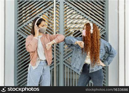 front view female friends with face masks outdoors doing elbow salute
