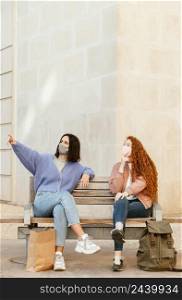 front view female friends with face masks outdoors sitting bench with copy space