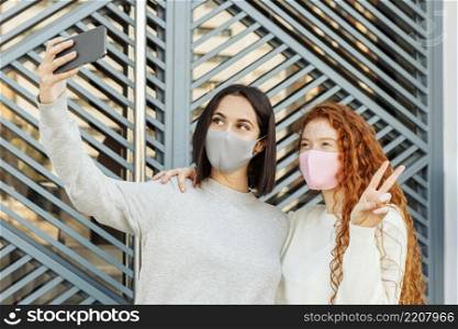 front view female friends with face masks outdoors taking selfie