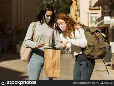 front view female friends with face masks outdoors with shopping bag