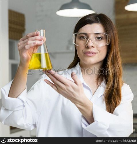 front view female scientist holding test tube while wearing safety glasses
