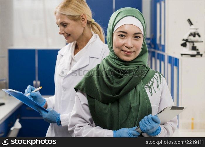 front view female scientist with hijab posing lab with colleague