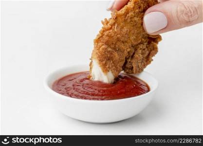 front view hand dipping fried chicken ketchup