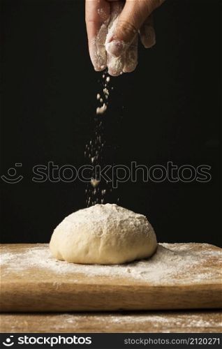 front view hand sprinkling flour dough cutting board