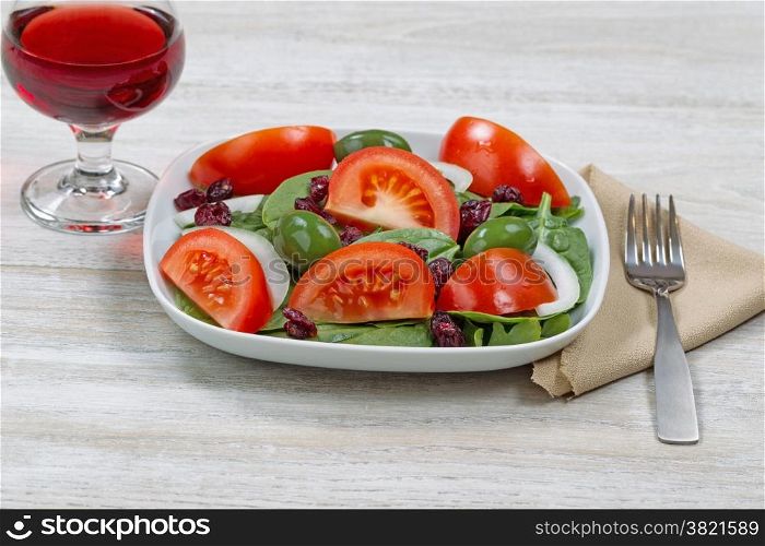 Front view image of a freshly made spinach salad in white plate with a glass of red wine and fork with cloth napkin on white wood