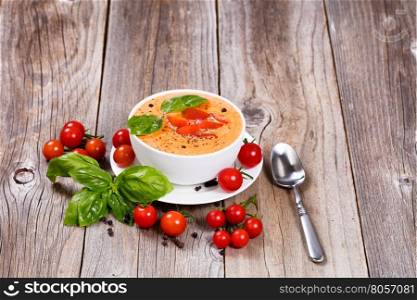 Front view of a fresh bowl of creamy tomato soup with cherry tomatoes and basil on rustic wooden boards.