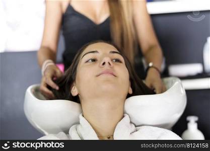 Front view of a hairdresser washing hair of a beautiful young woman in hair salon.
