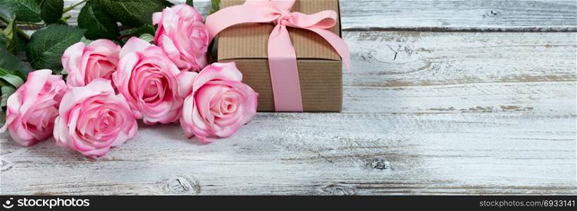 Front view of a half a dozen pink roses and gift box on rustic white wood in flat lay view