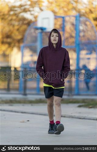 Front view of a young hooded teen male walking away