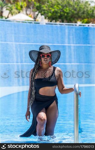 Front view of an African-American woman wearing swimwear exiting the pool by the ladder. Adult woman enjoying a summer day in pool.. Front view of an African-American woman wearing swimwear exiting the pool by the ladder