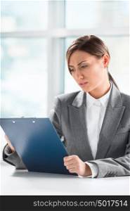 Front view of business woman looking over papers on clipboard at her office