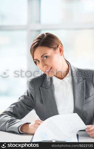 Front view of business woman looking over papers on clipboard at her office