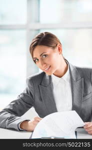 Front view of business woman looking over papers on clipboard at her office