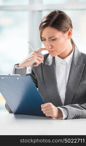 Front view of business woman looking over papers on clipboard at her office