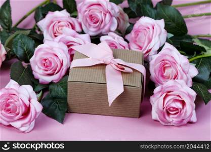 Front view of light pink rose flowers and giftbox forming on a pink background for Mothers Day or Valentines holiday concept