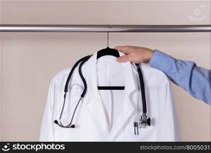 Front view of medical doctor hand reaching for hanging consultation white coat with stethoscope and pens.