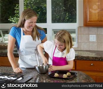 Front view of mother watching her younger daughter mixing up the raw cookie dough