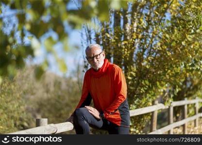 Front view of one senior runner man with sportswear sitting on a wooden fence while looking camera