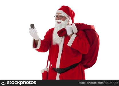 Front view of Santa Claus looking at mobile phone while carrying sack of Christmas presents over white background