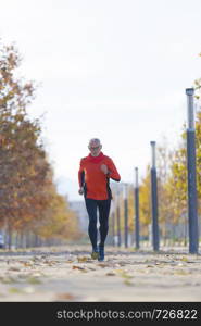 Front view of senior man in sport clothes jogging in a city park in a sunny day