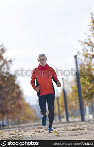 Front view of senior man in sport clothes jogging in a city park in a sunny day