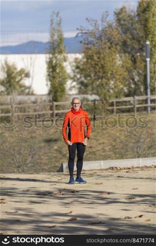 Front view of senior man in sport clothes standing in a city park in a sunny day
