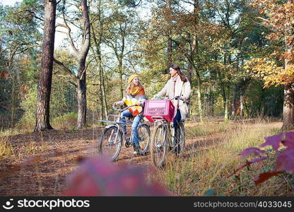 Front view of teenage girls walking in forest pushing bicycles