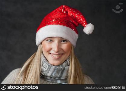 Front view of the smiling blond female in Santa hat. Pretty blond wearing christmas hat on dark background