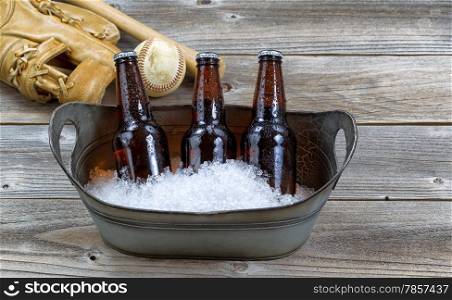 Front view of three brown bottled beers, crushed ice in metal bucket, and baseball equipment in background on rustic wood
