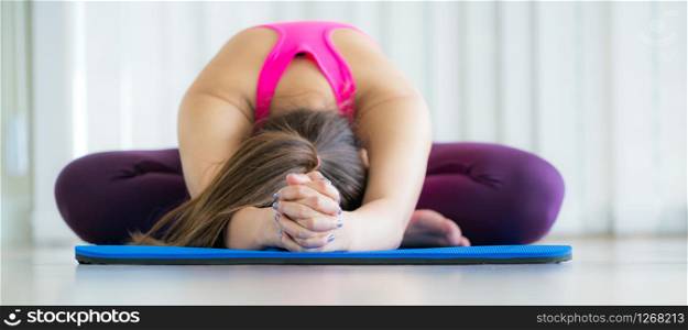 Front view of young woman exercising stretching back yoga pose on mat in an indoor gym with copy space. Healthy lifestyle and wellness concept.