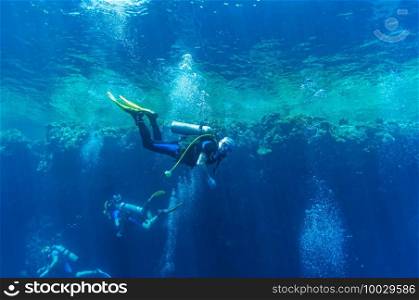 Front view on scuba divers group swimming who exploring deep dark ocean blue water against the backdrop of a coral reef. Male and female in flippers examines the seabed. Air bubbles. Active life.Dive.. Front view on scuba divers group swimming who exploring deep dark ocean blue water against the backdrop of a coral reef. Male and female in flippers examines the seabed. Dive. Active life.Air bubbles.