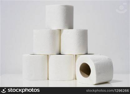 Front view on white toilet paper rolls stacked on the table in front of the wall background