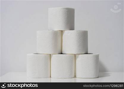 Front view on white toilet paper rolls stacked on the table in front of the wall background