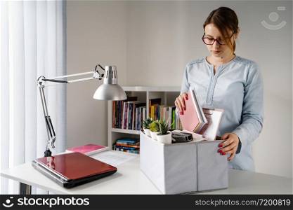 Front view on young caucasian woman female girl standing by the table at the office at work packing personal items stuff in the box after being fired from work dismissed job quit due crisis recession