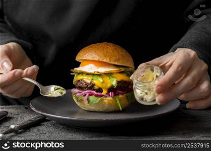front view person near burger plate holding jar with butter