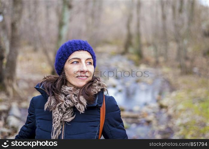Front view portrait of beautiful girl with backpack standing near old footbridge. She is having break during hike in coniferous forest