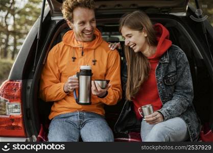 front view smiley couple enjoying hot beverage trunk car