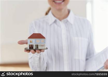 front view smiley defocused female realtor showing miniature house