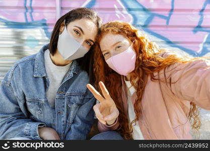 front view smiley female friends with face masks outdoors taking selfie